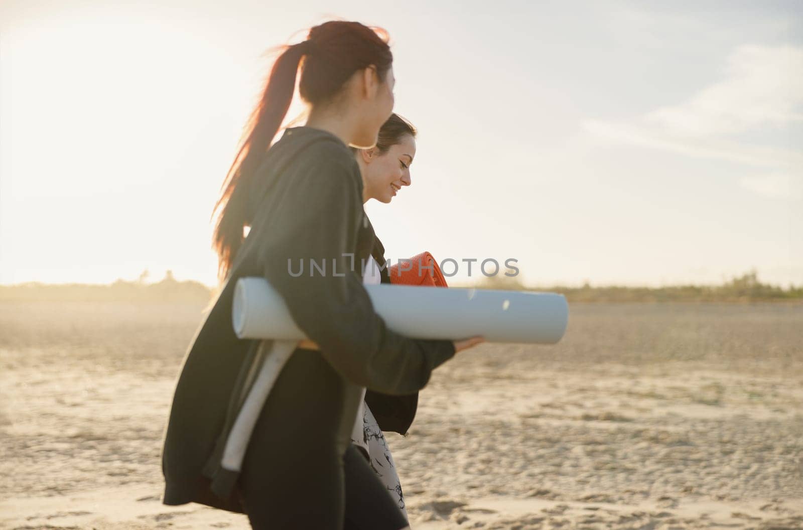 Two fit women walking on the beach with their yoga mats after doing morning gym. High quality photo