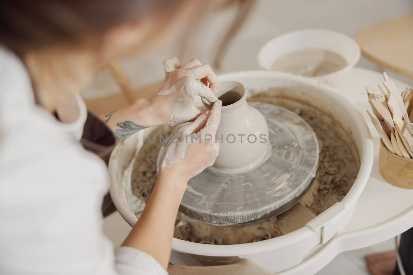 Female potter in apron making shape of clay vase on spinning pottery tool in ceramic workshop by Yaroslav_astakhov