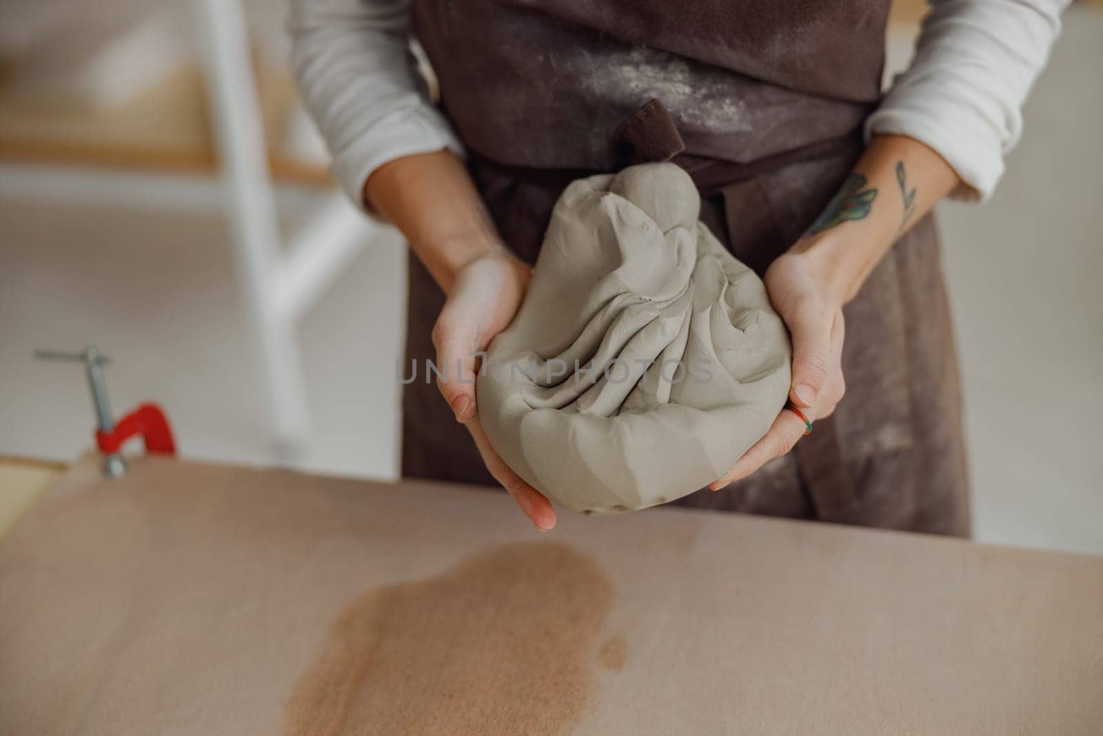 Close up of woman preparing clay to create a mug on a wooden table in pottery studio by Yaroslav_astakhov