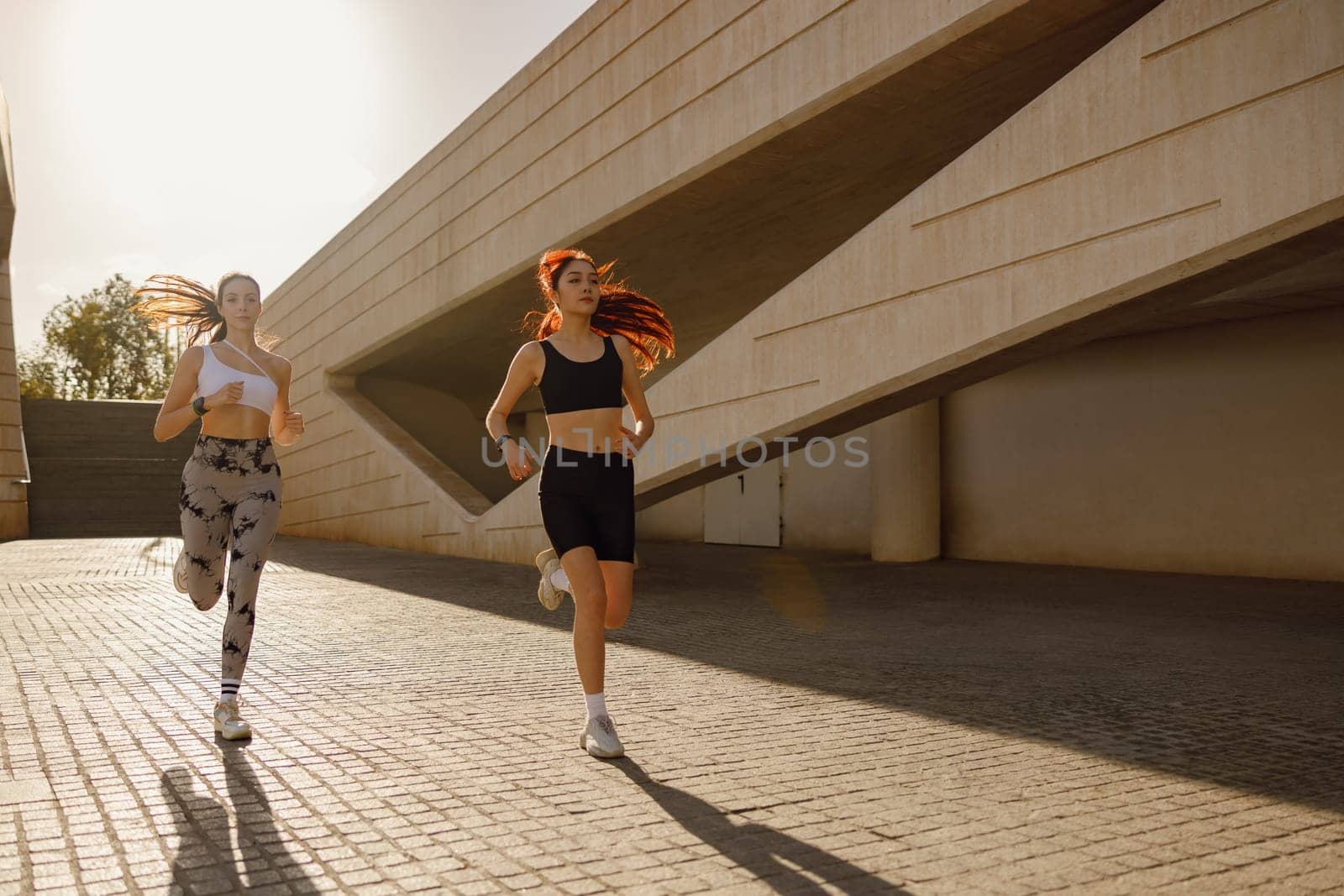 Active women athlete running on sunny morning side by side on modern building background by Yaroslav_astakhov