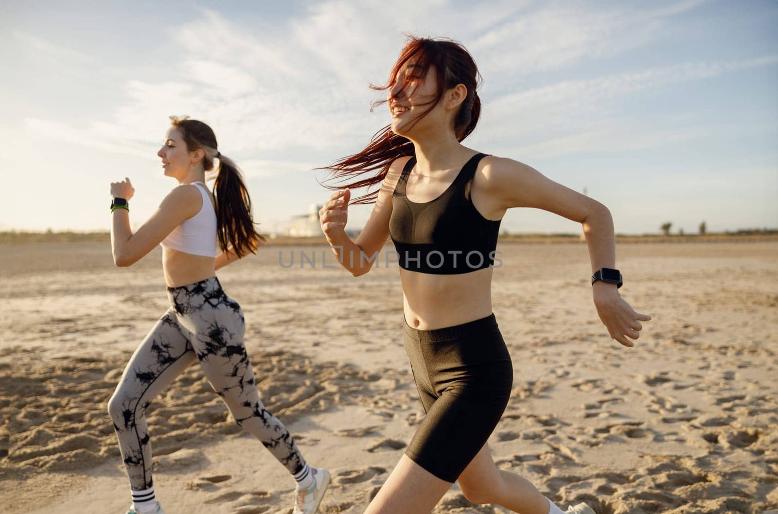 Young female friends in sportswear running on beach in morning sunrise. Outdoor workout routine by Yaroslav_astakhov