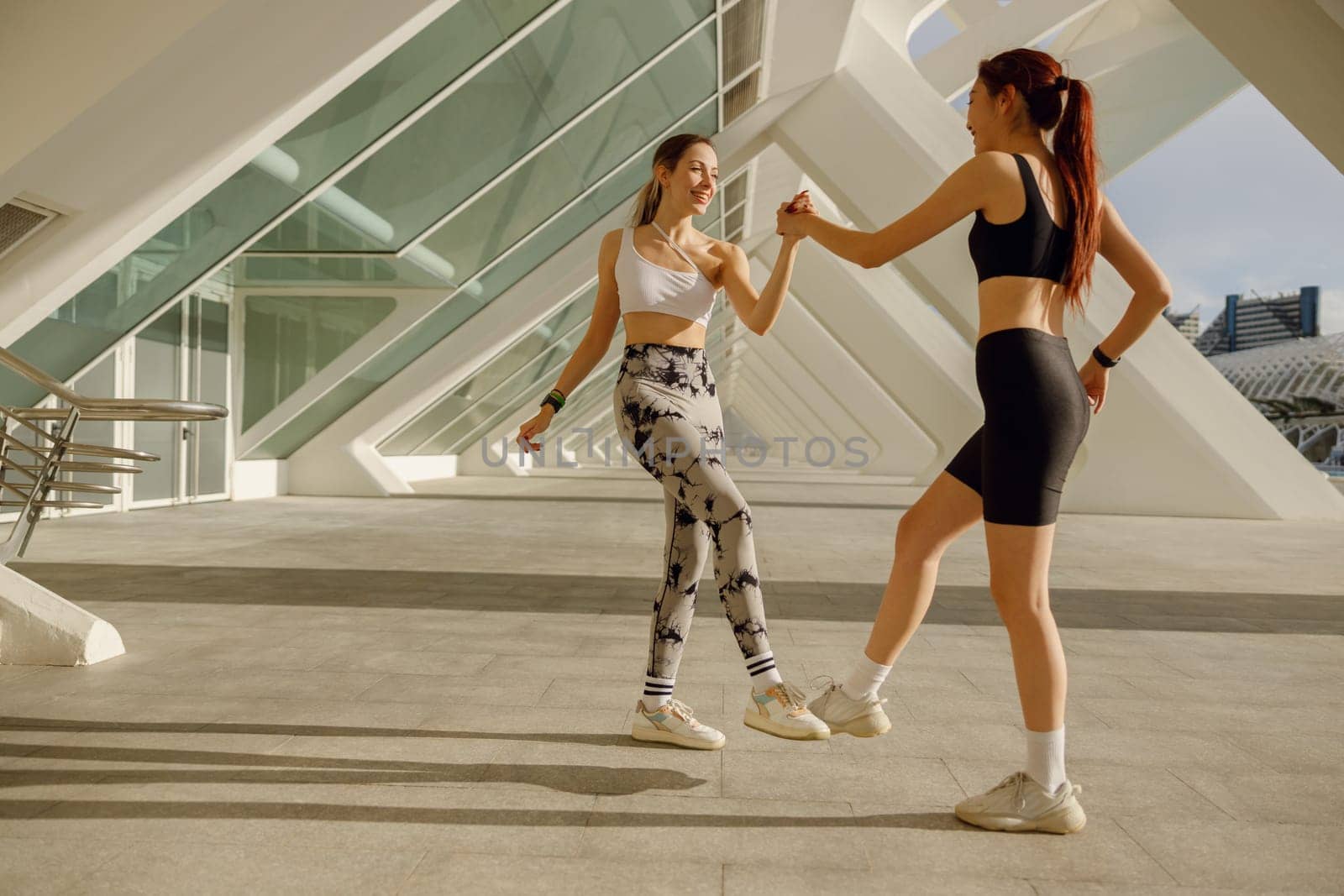 Happy female friends doing gesture of sport shake hand and legs after exercising outside by Yaroslav_astakhov