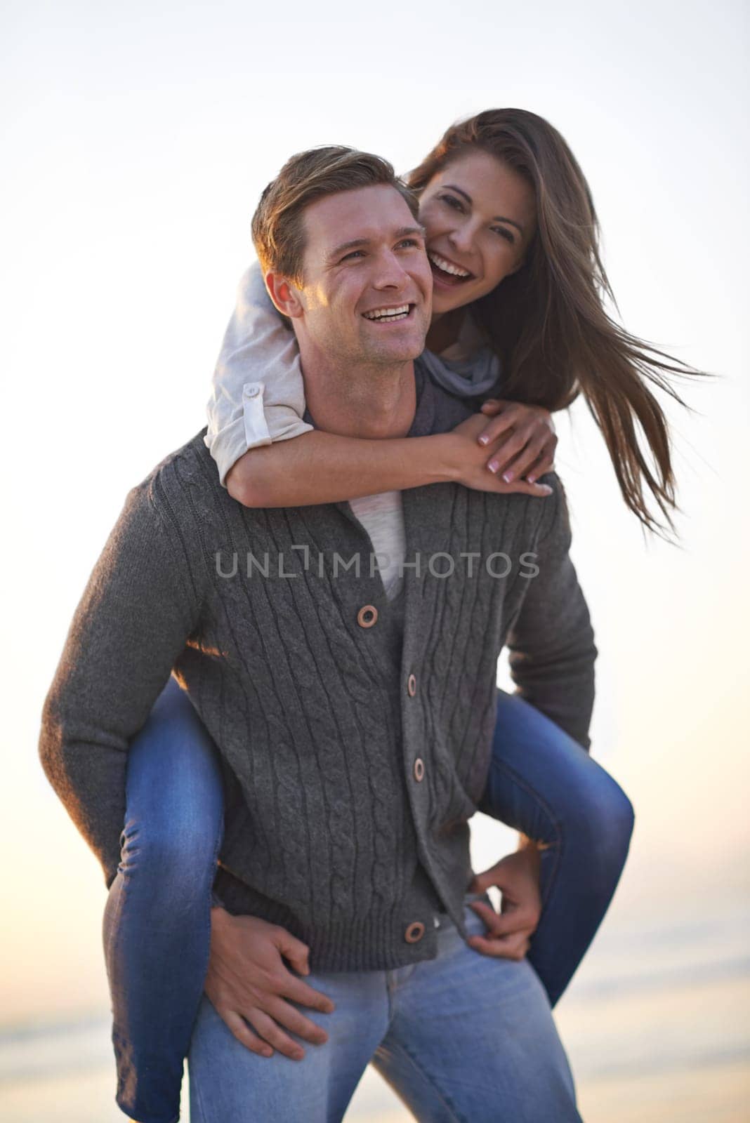 Portrait, piggy back and happy couple on beach at sunset for tropical holiday adventure, relax and bonding together. Love, man and woman on romantic date with ocean, evening sky and travel vacation. by YuriArcurs