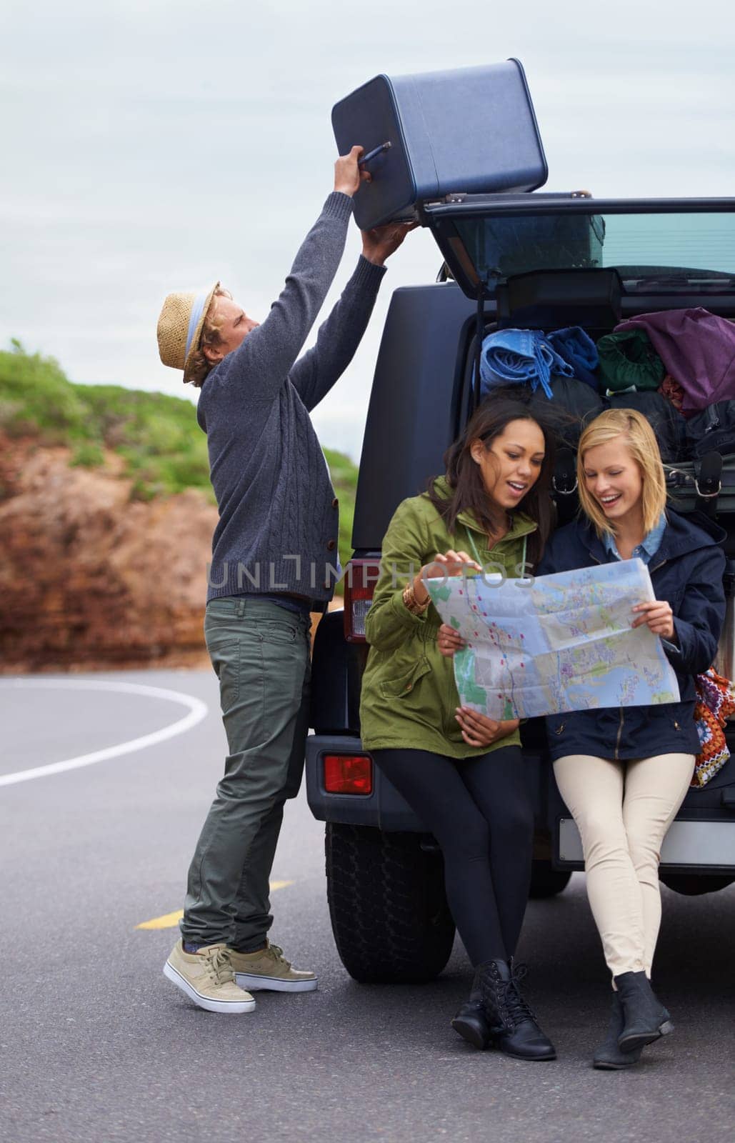 Happy woman, friends and map with a car full of luggage for road trip, destination or planning outdoor vacation. Group of young people checking travel guide and packing bags for adventure or journey.