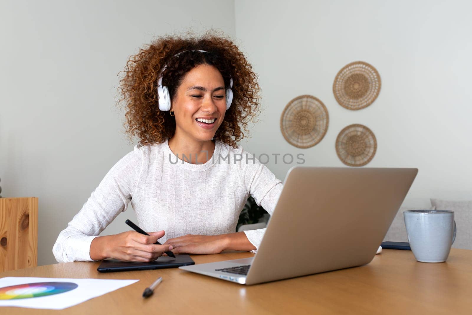 Multiracial happy female graphic designer working at home using laptop and graphic tablet. Creativity and technology concept.