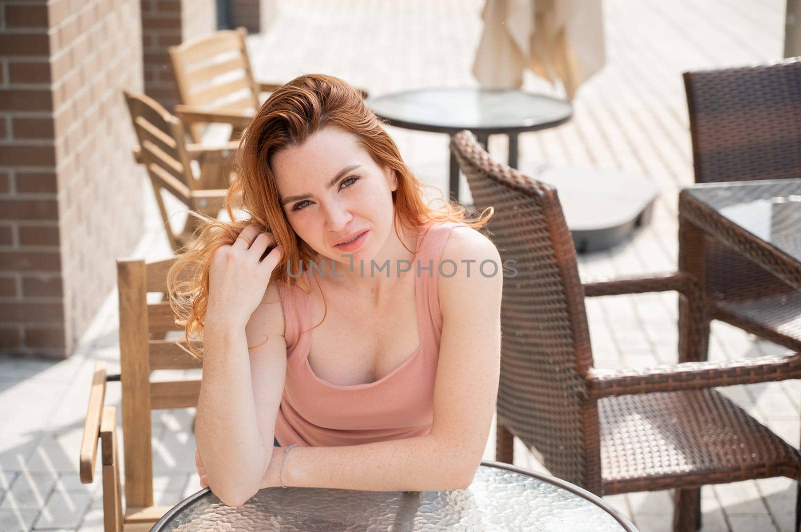 Beautiful young red-haired woman with braces on her teeth smiling while sitting in an outdoor cafe. by mrwed54