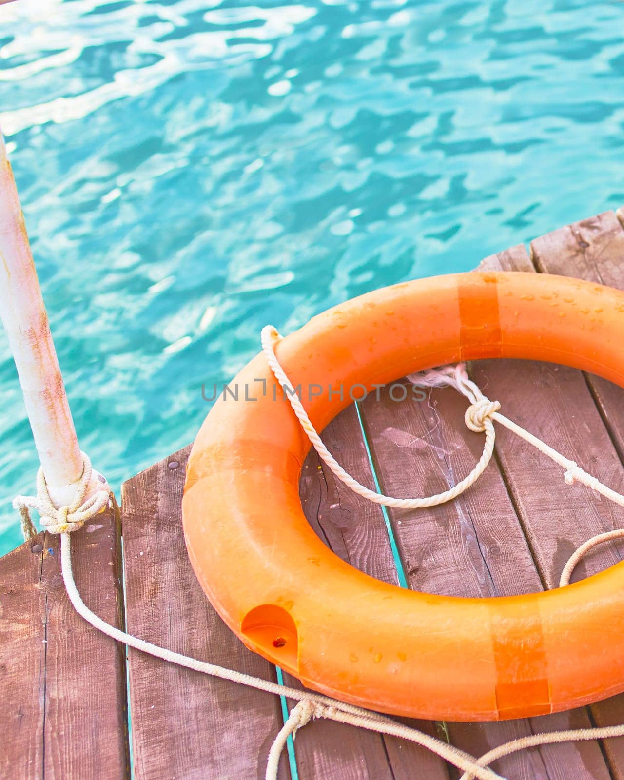 Orange lifebuoy with rope on a wooden pier near sea. Close up of lifebuoy on wooden pier at the beach.