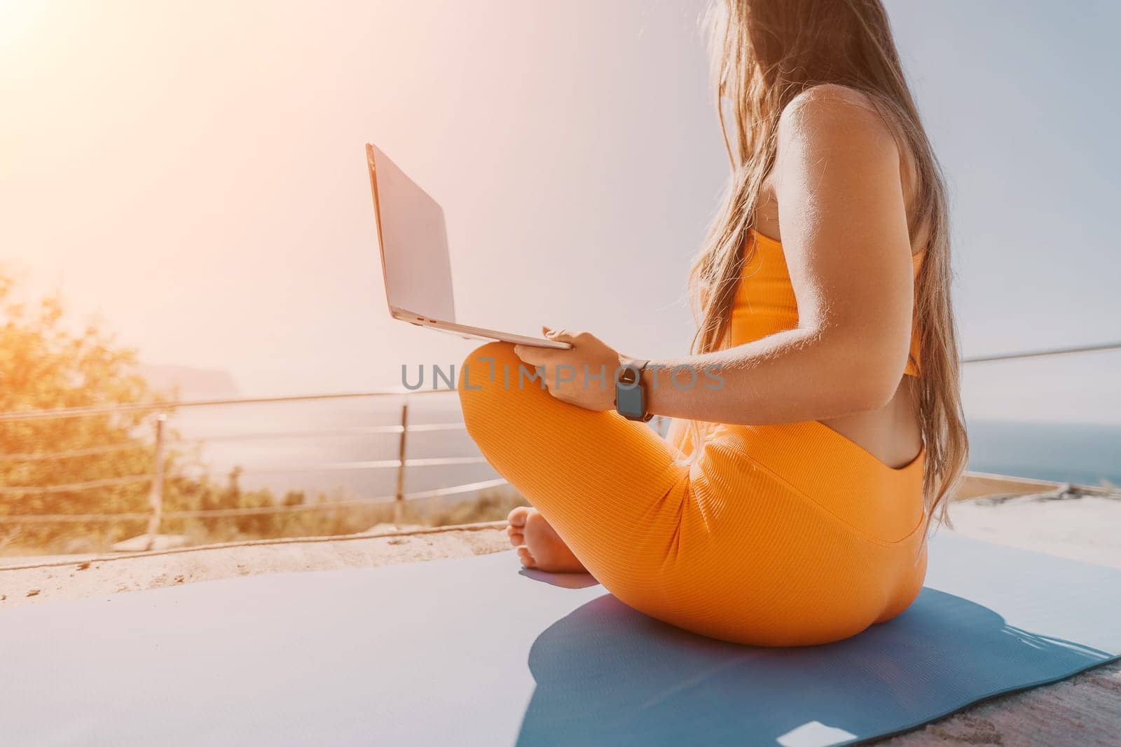 Digital nomad, Business woman working on laptop by the sea. Pretty lady typing on computer by the sea at sunset, makes a business transaction online from a distance. Freelance, remote work on vacation