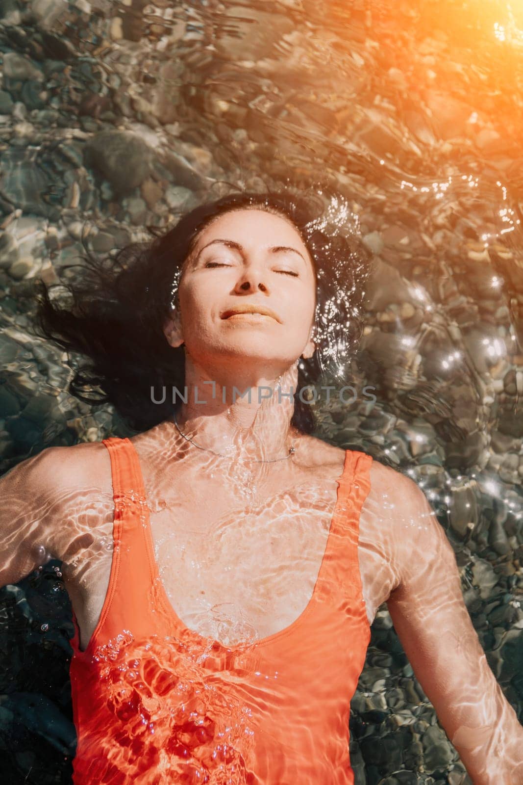 Woman travel portrait. Close-up portrait of a happy woman with long hair in a red bikini, floating in water and smiling at the camera. by panophotograph