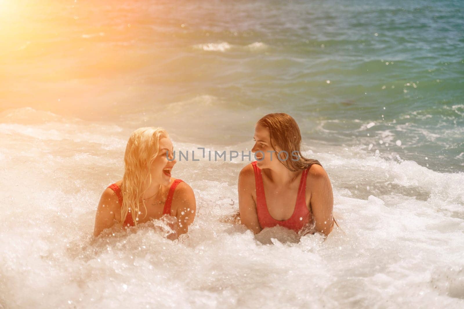 Women ocean play. Seaside, beach daytime, enjoying beach fun. Two women in red swimsuits enjoying themselves in the ocean waves. by Matiunina