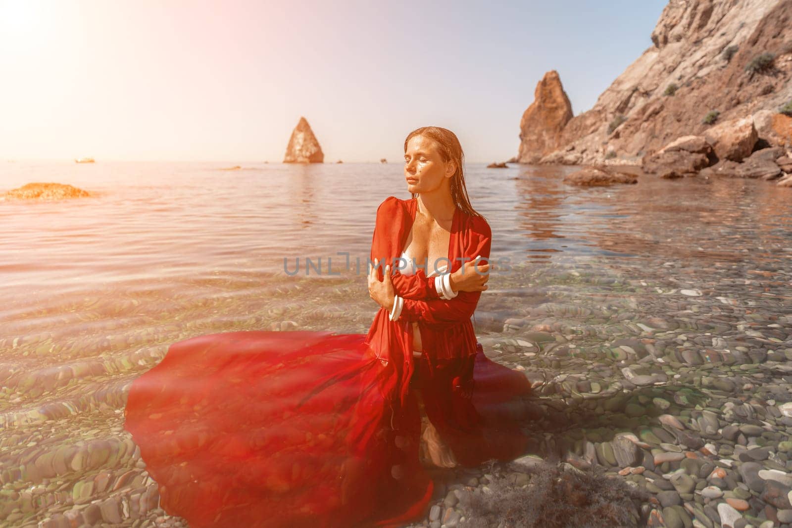 woman sea red dress. Beautiful sensual woman in a flying red dress and long hair, standing in sea in a large bay. by Matiunina