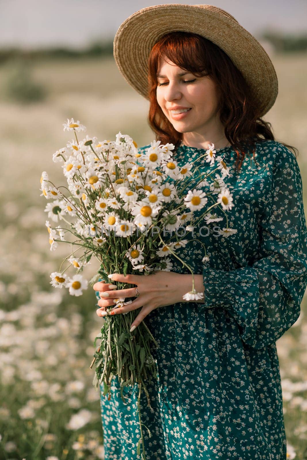 Happy woman in a field of daisies with a wreath of wildflowers on her head. woman in a green dress in a field of white flowers. Charming woman with a bouquet of daisies, tender summer photo.