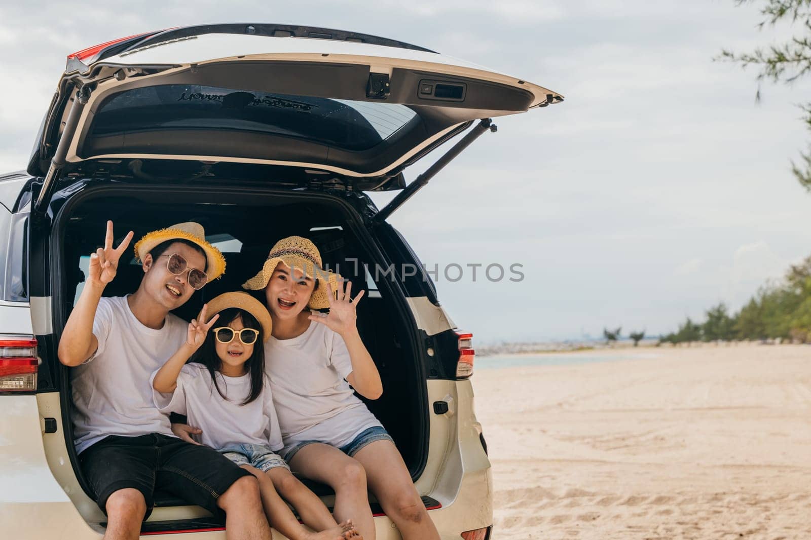 Happy Family Day. Dad, mom and daughter enjoying road trip sitting on back car show V-sign finger, Parents and children traveling in holiday at sea beach, family having fun in summer vacation on beach