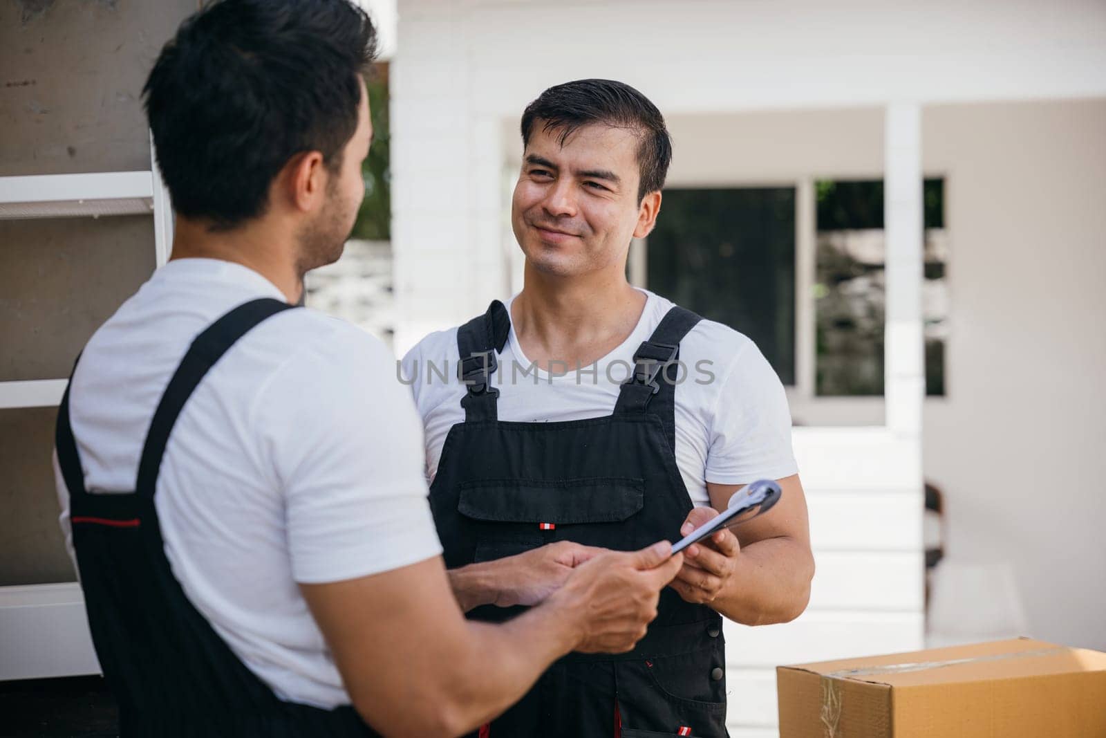 Moving service workers outdoors unloading boxes and checking list for the relocation company. Their teamwork guarantees a smooth and efficient move. Moving Day