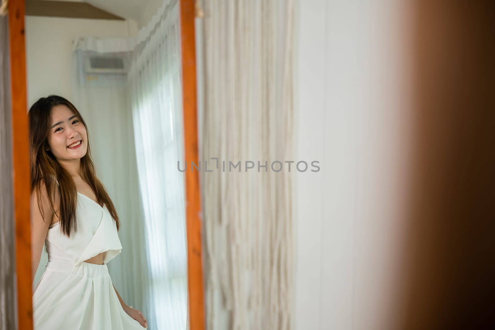 Cute woman wearing dress on front mirror looking clothes at home after morning wake up, Beautiful young female trying on blouse and smiling standing in front mirror in room, beauty fashion lifestyle