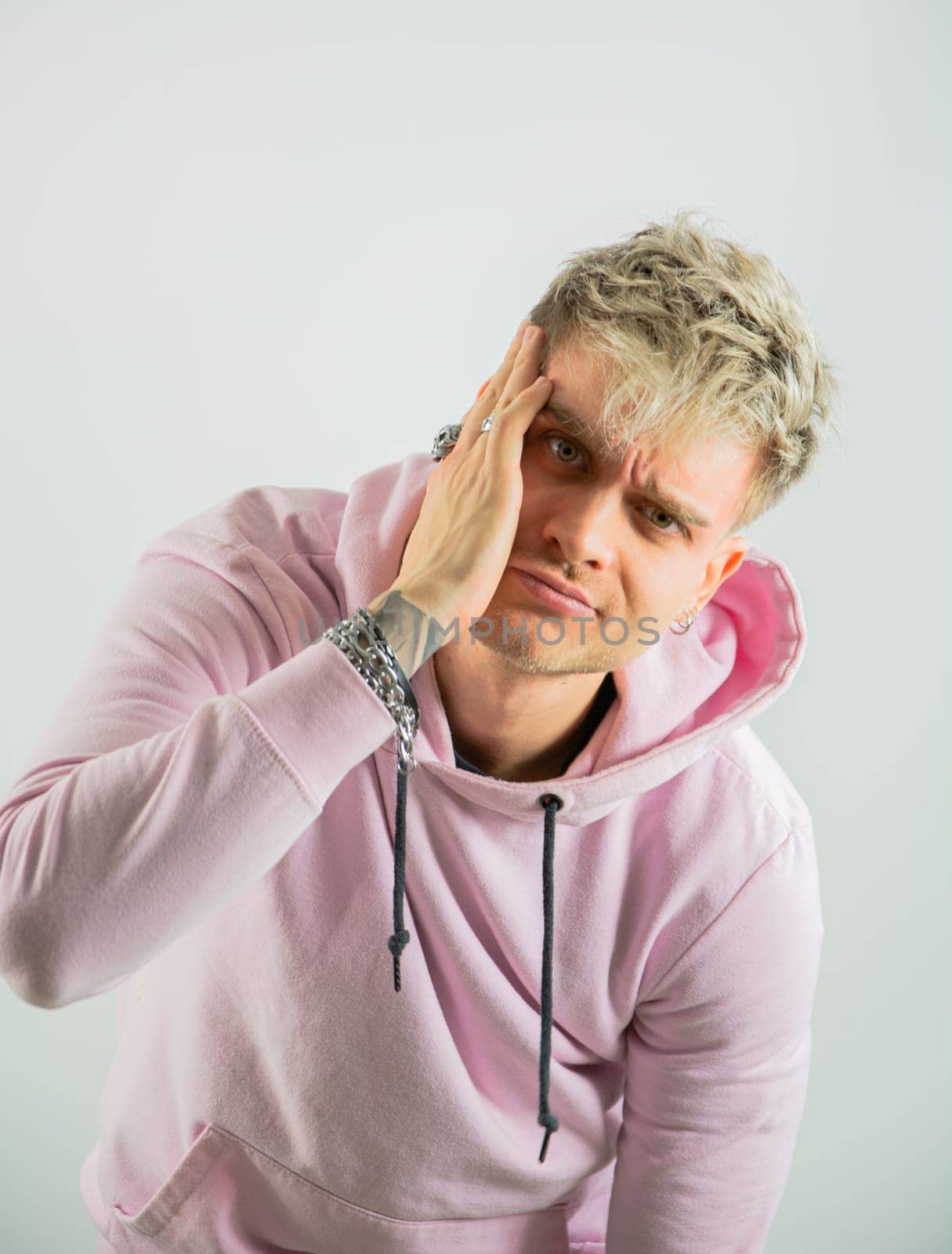 A photo of a man wearing a pink hoodie holding his head with his hands, appearing distressed or overwhelmed. He is seated or standing in an unspecified location.