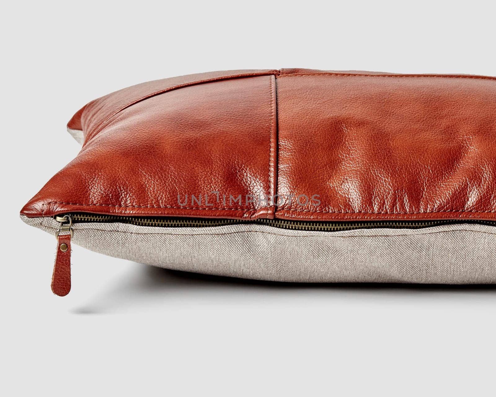 Stylish sofa pillow with hand-stitched brown leather squares on front, grey linen back and side zipper on white background. Concept of comfort and quality of handcrafted product