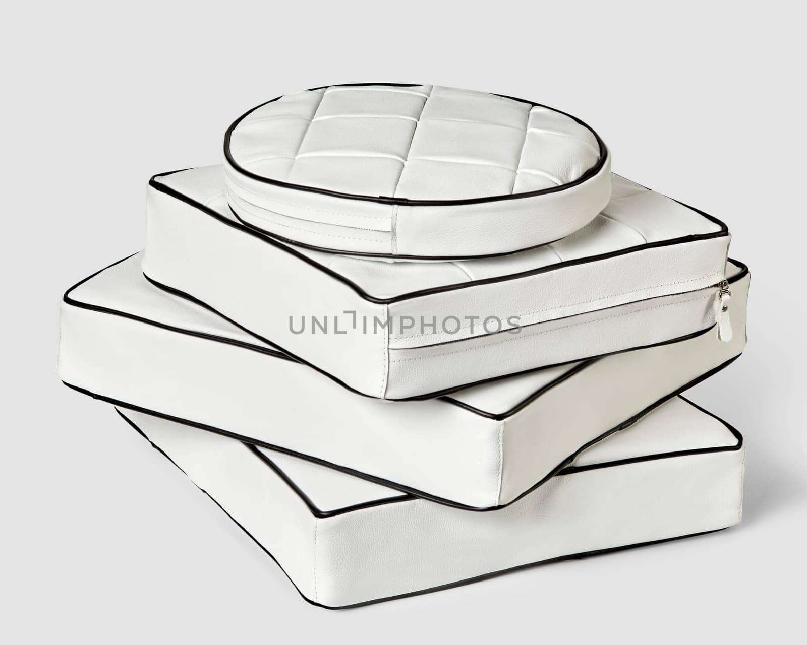 Stack of stylish minimalist square and round seat cushions of different sizes in white genuine leather decorated with black trim. Handmade interior accessories