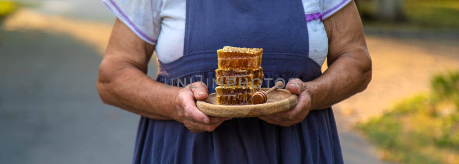 An elderly woman holds honey in her hands, selective focus. People.