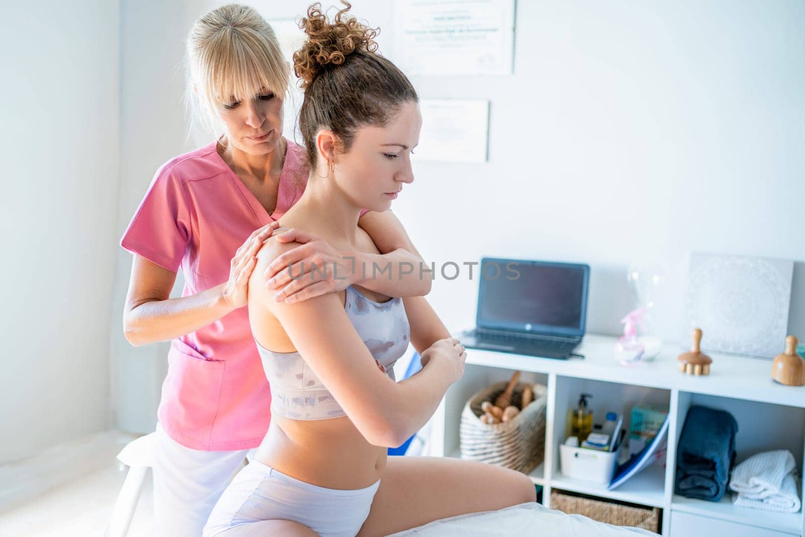 Focused osteopath massaging back of female client sitting on bed in clinic by javiindy