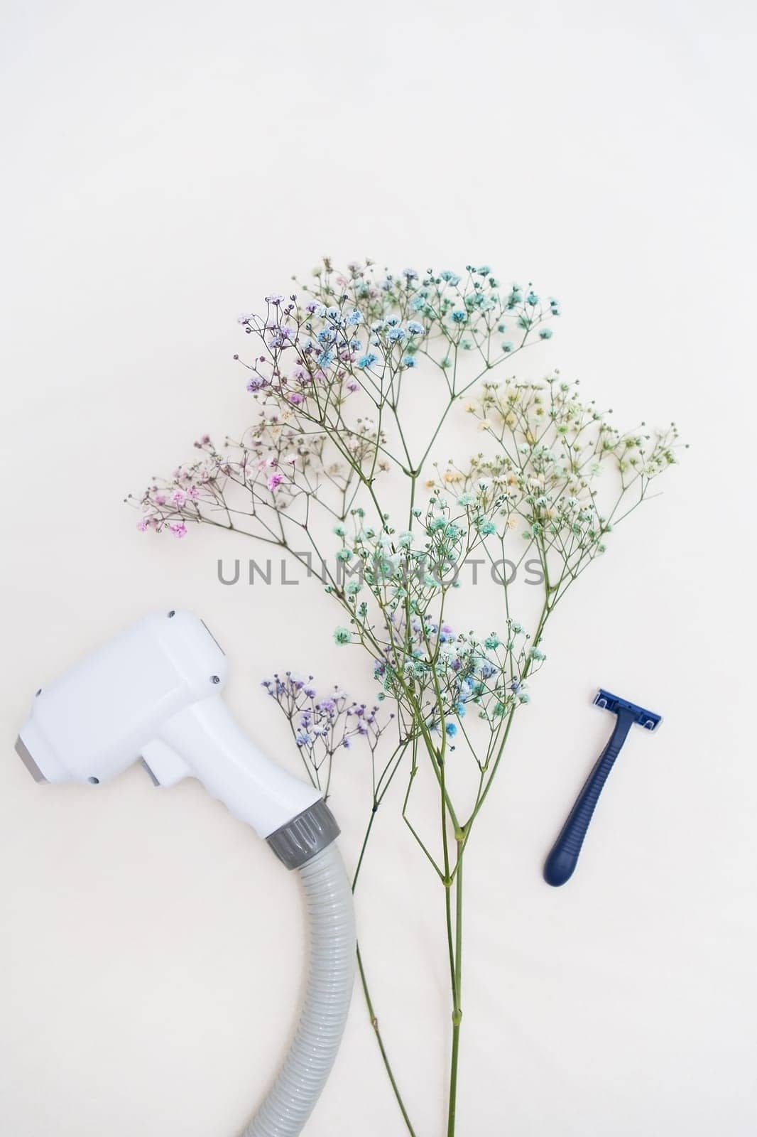 A laser hair removal machine and a razor are juxtaposed with delicate flowers on a light background, symbolizing the contrast between modern technology and the standard method of hair removal. by sfinks