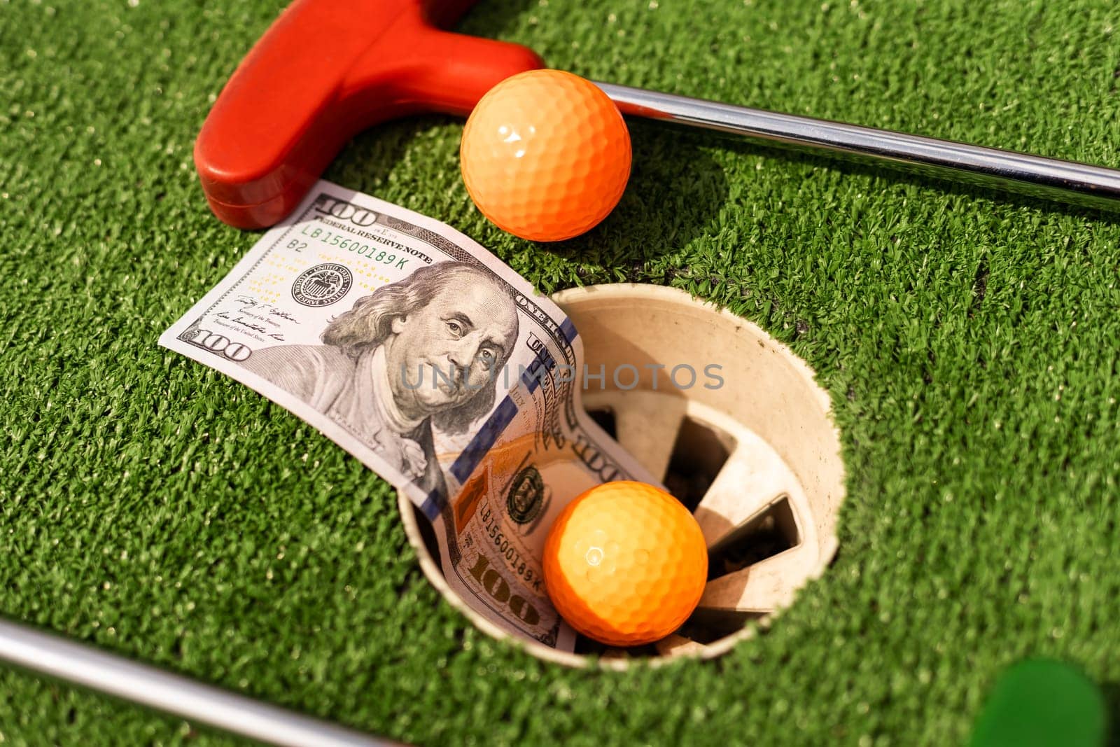 Mini Golf club, ball and money on the artificial grass by Andelov13