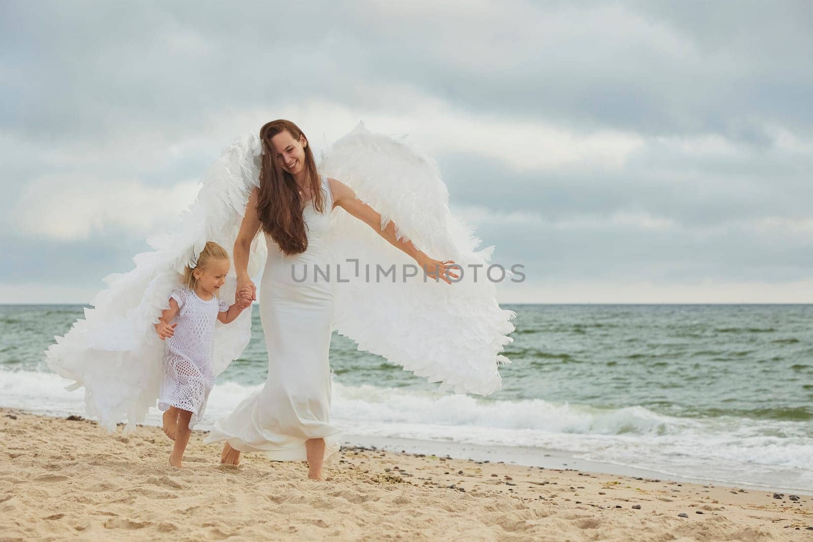Sondervig, Denmark, August 22, 2023: Mom and daughter dressed as angels on the sea at sunset