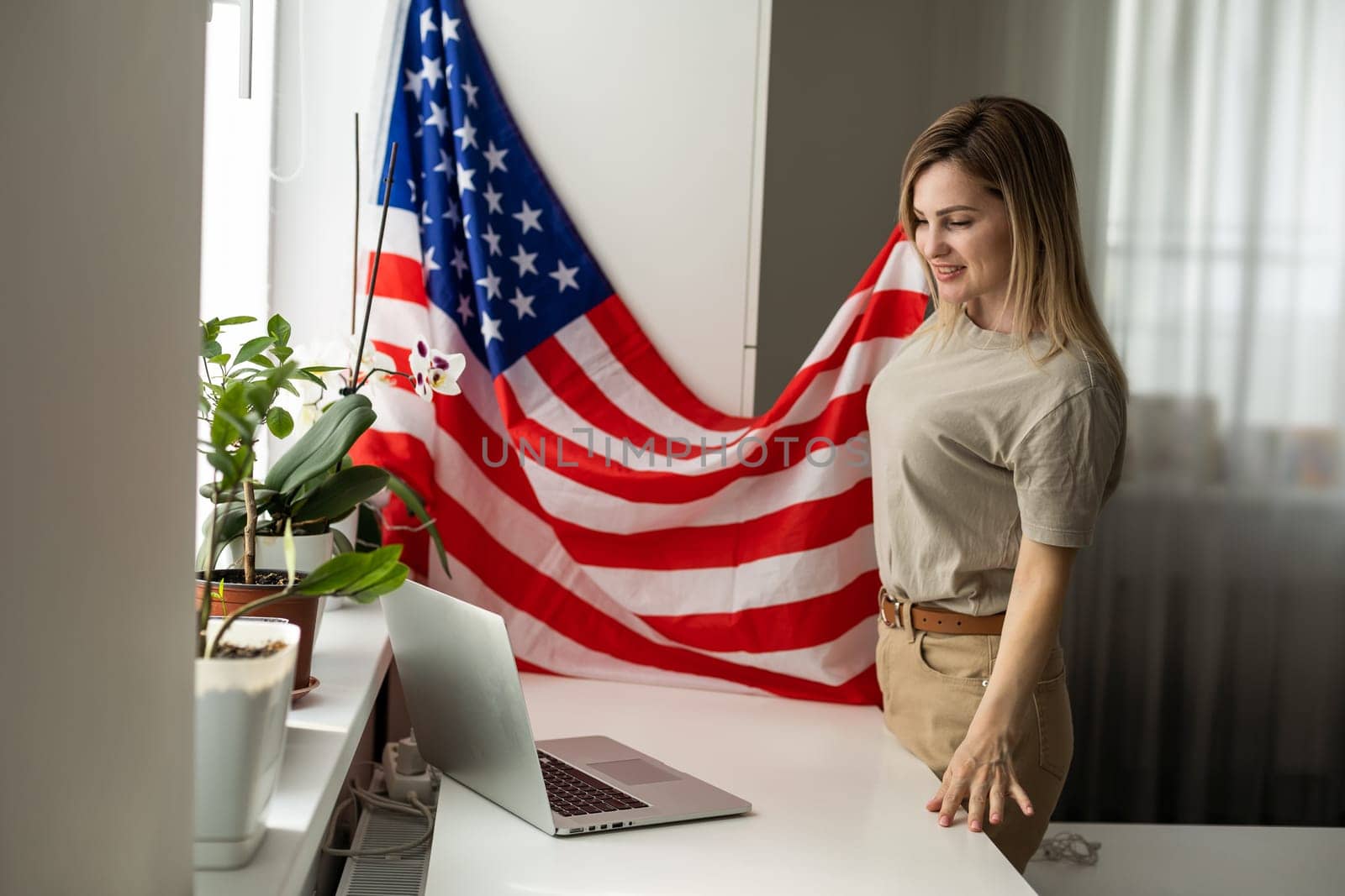 Happy woman employee sitting wrapped in USA flag, shouting for joy in office workplace, celebrating labor day or US Independence day. High quality photo