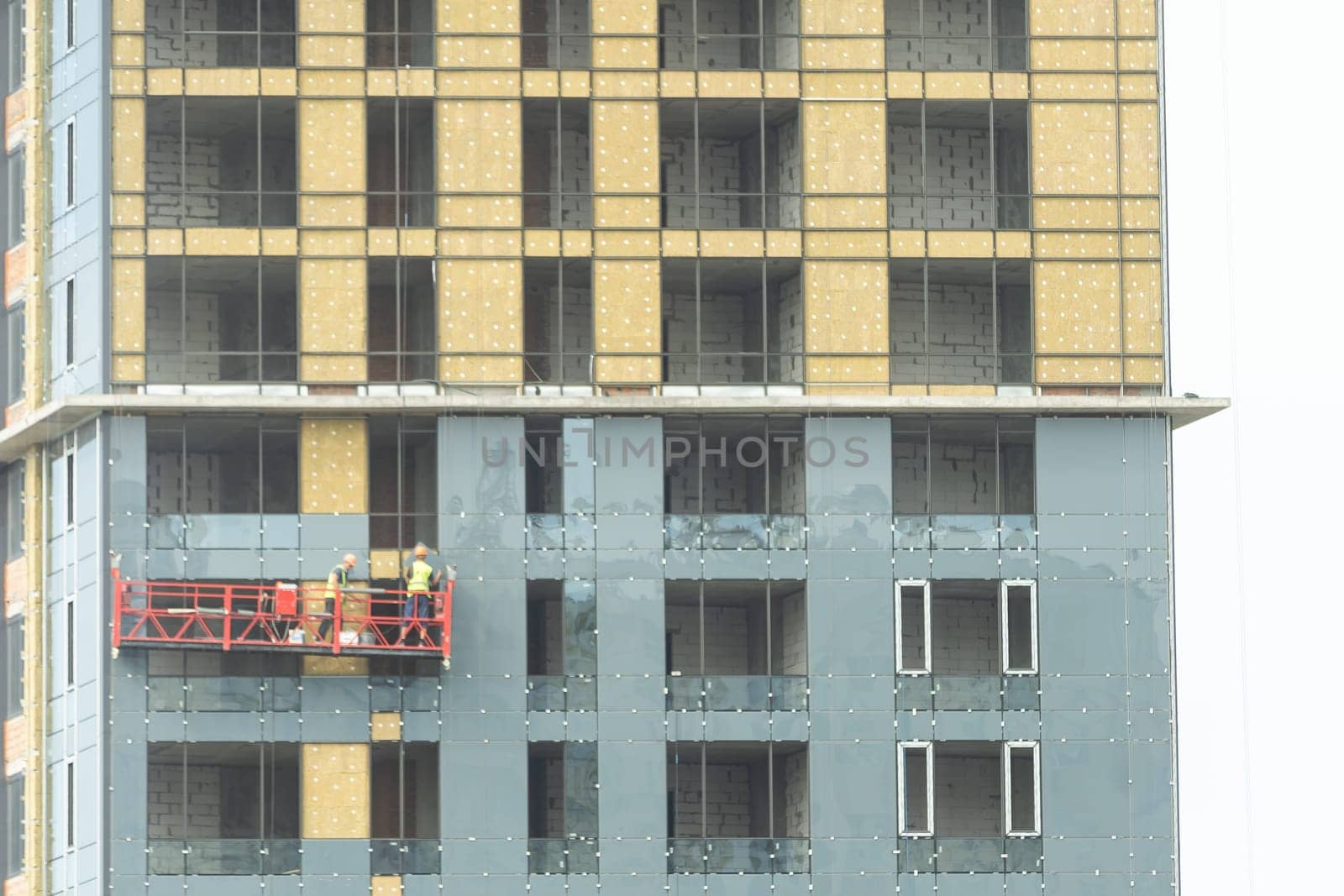 Construction cradle on a building at a height with workers. Work at height in a construction cradle by Andelov13