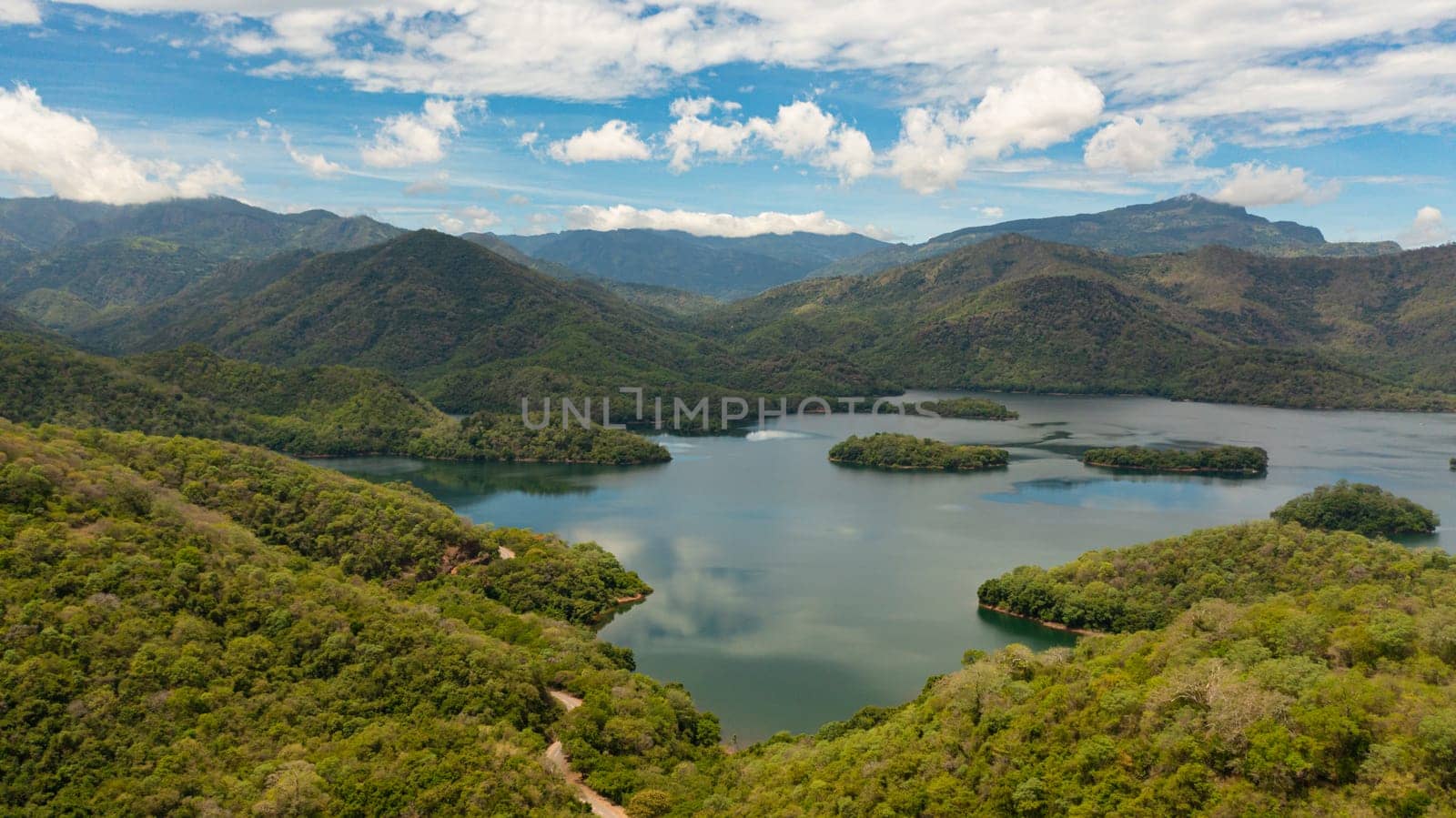 Aerial view of mountain lake among hills with tropical vegetation and blue sky with clouds. Randenigala reservoir, Sri Lanka.