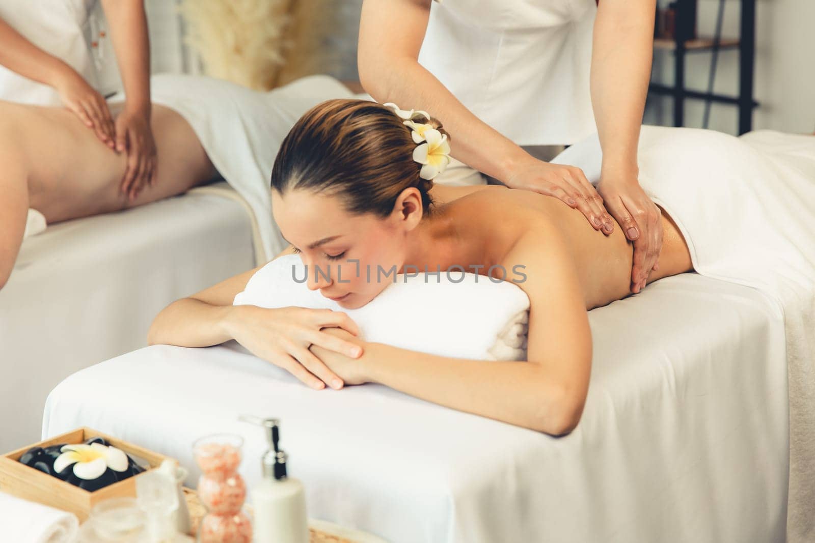 Caucasian couple customer enjoying relaxing anti-stress spa massage and pampering with beauty skin recreation leisure in day light ambient salon spa at luxury resort or hotel. Quiescent