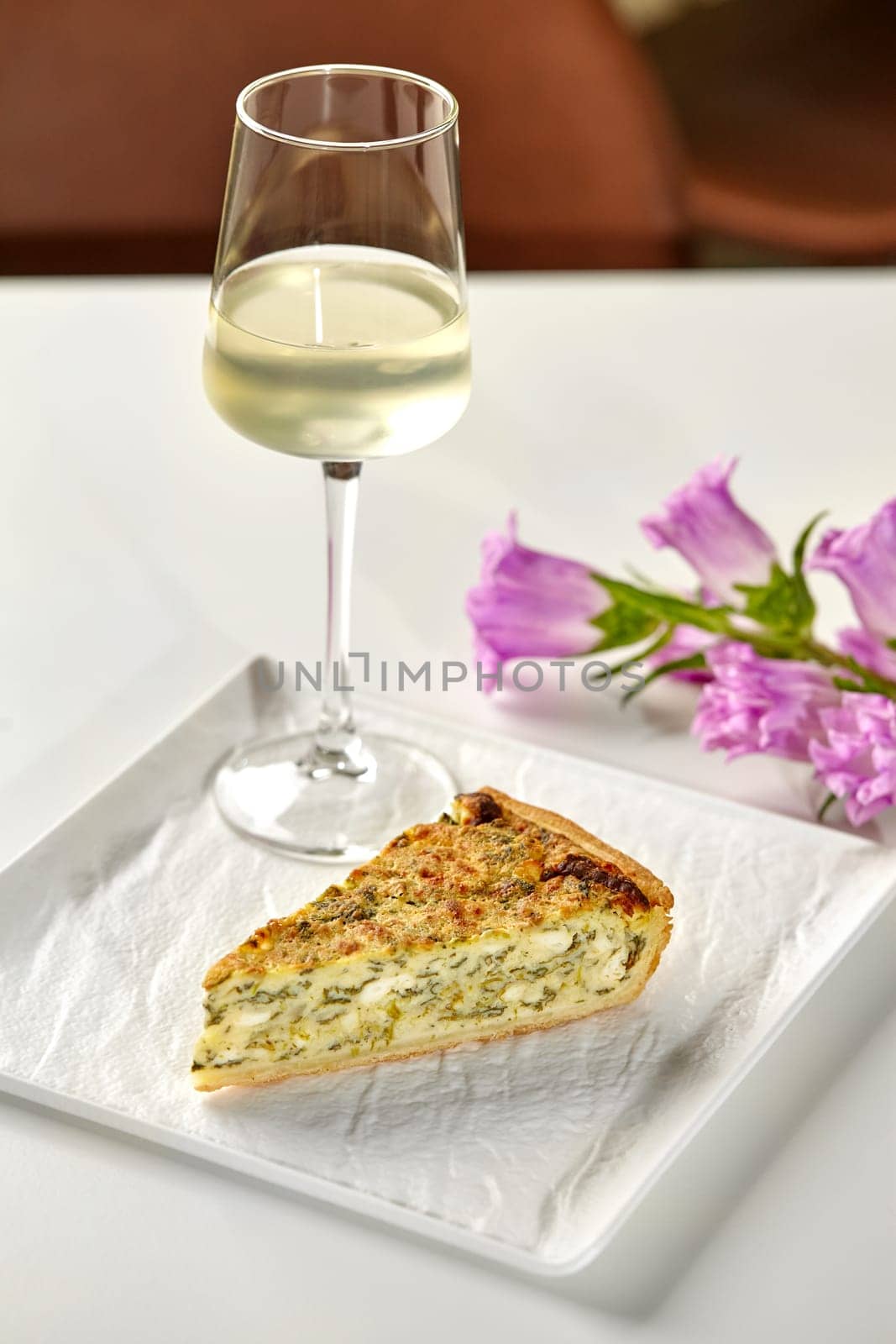 Piece of cheese and spinach quiche with wine and flowers by nazarovsergey
