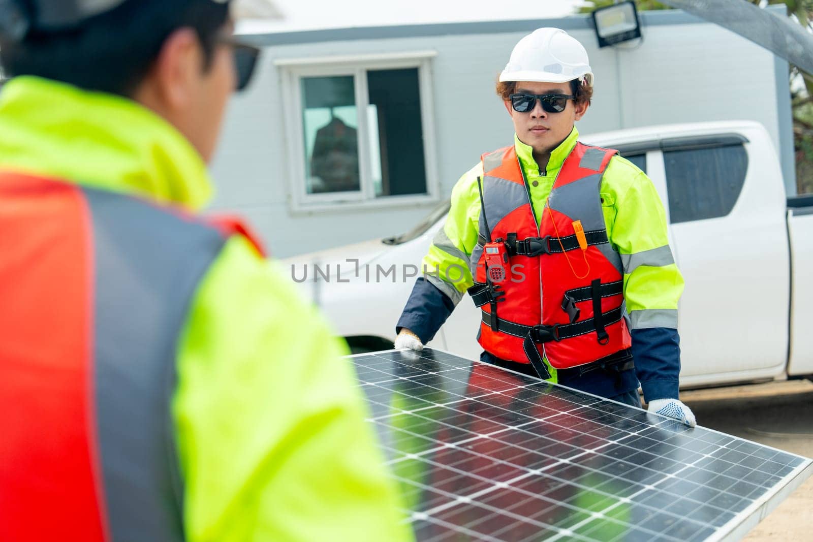 Two professional technician workers help to carry solar cell panel to area of workplace.
