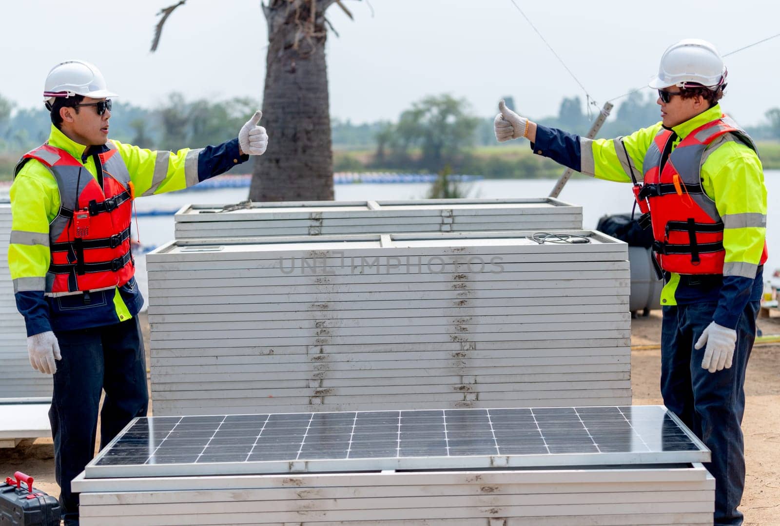 Two Asian technician worker stand beside solar cell panel and show thumbs up to each other in concept of green energy system and success of work.