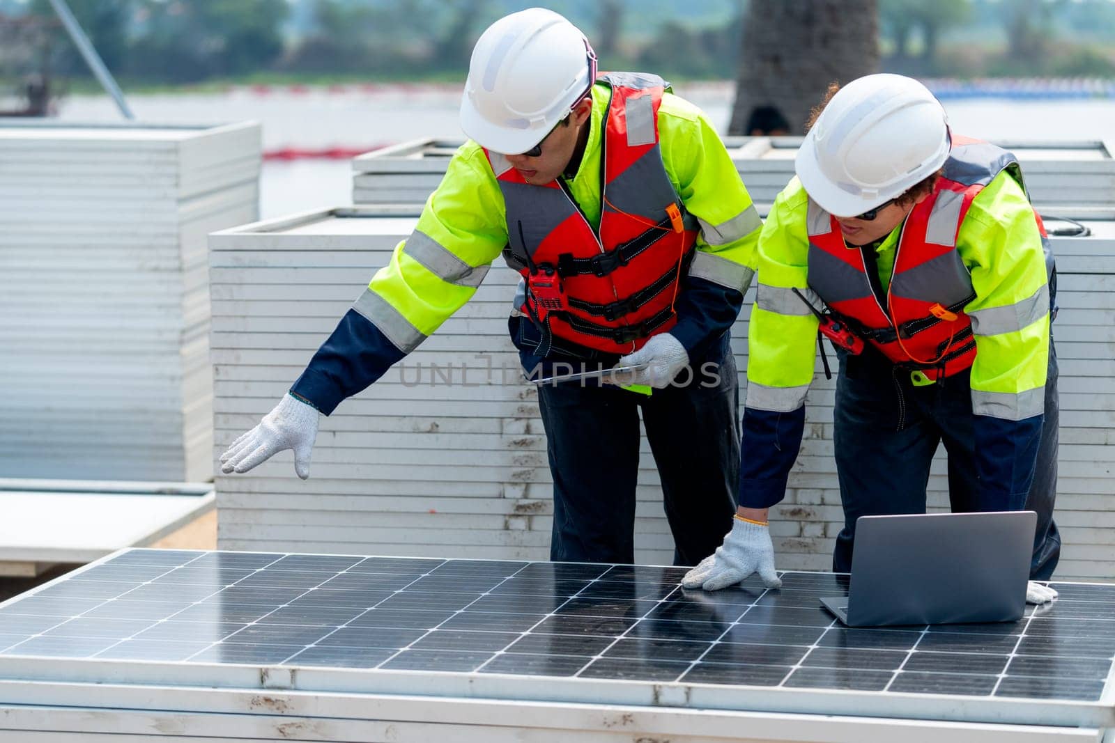 Two Asian professional technician workers stand near solar cell panel and use laptop to discuss about work in concept of green energy system for good environment.