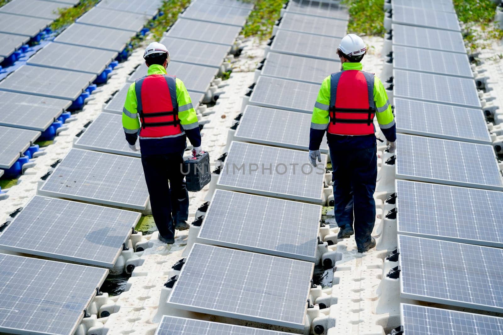 Back of professional with safety uniform walk on footpath along row of solar cell panels in workplace.