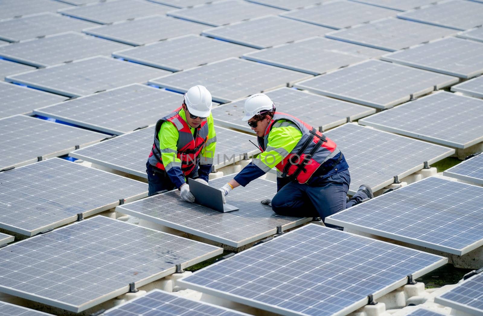 Two professional technician workers sit and work together using laptop in area of solar cell panel system in concept of green energy power plant.