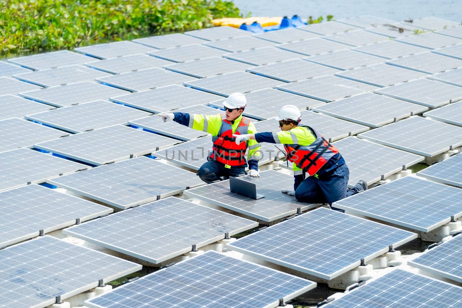 Two professional technician workers point together to the left and discuss about work with solar cell panel system in concept of green energy power for good environment.