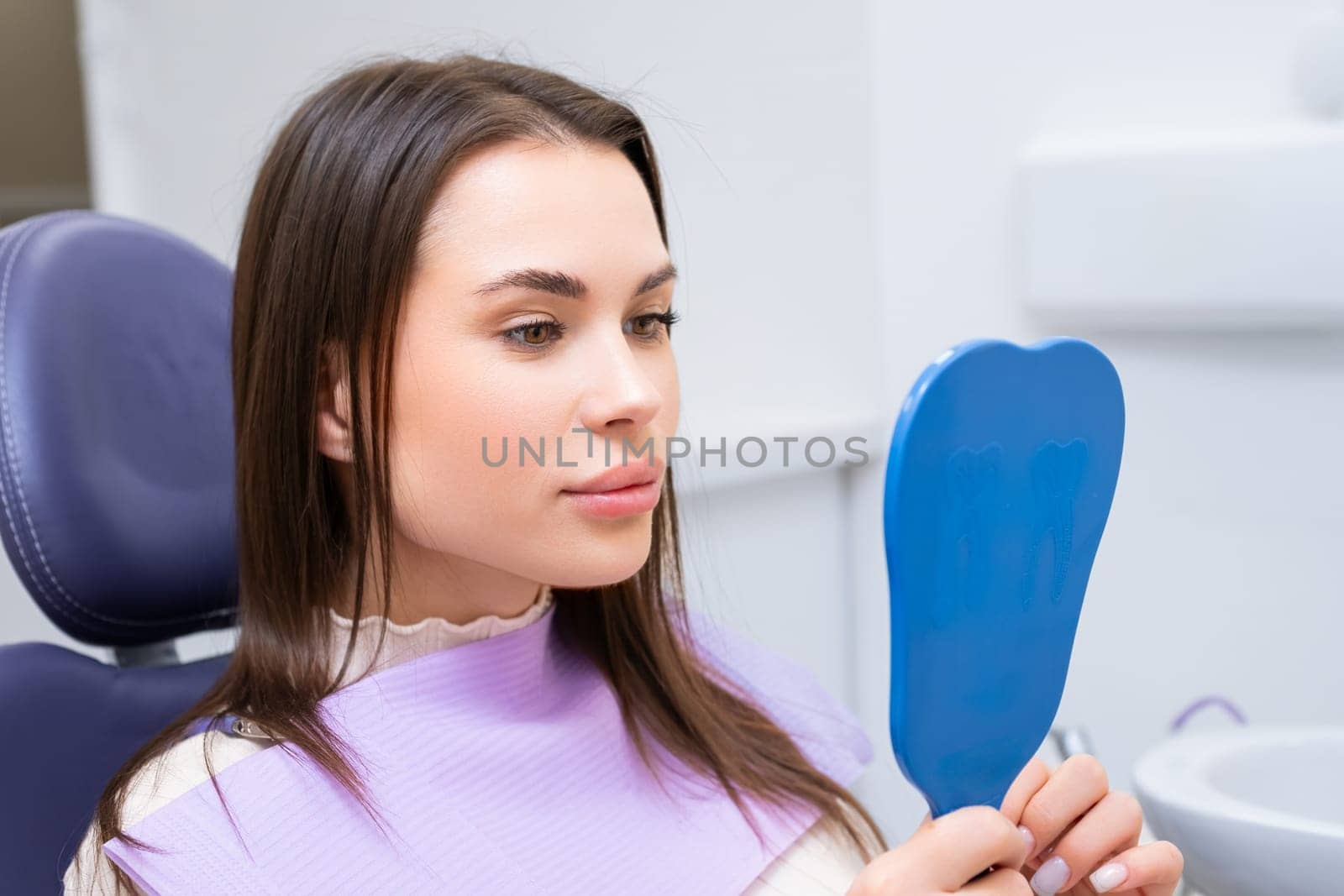 Brunette patient looks in the mirror in dental clinic after check up