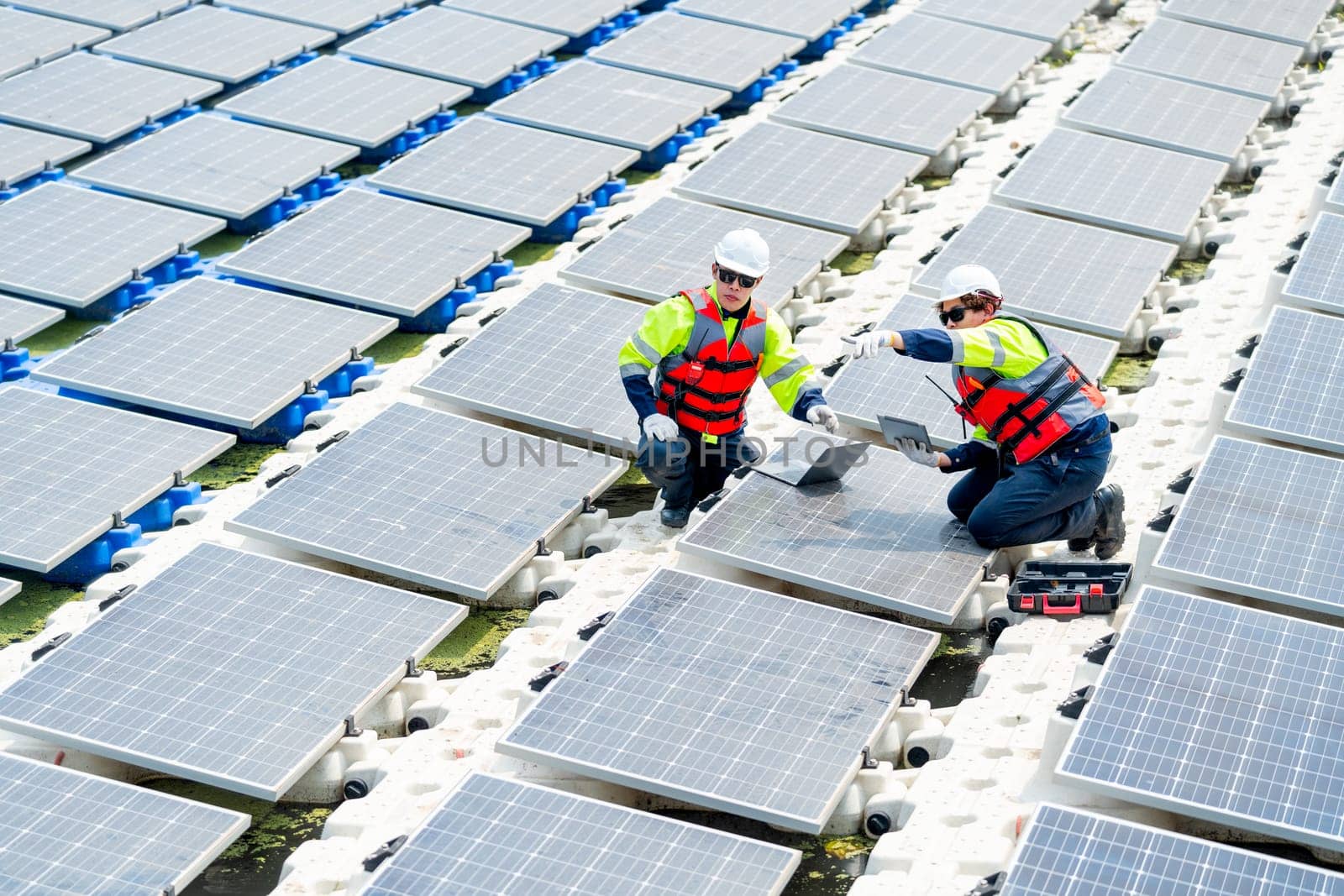 One professional technician worker sit and point to left side during work with solar cell panel and discuss with co-worker for working  over the water reservoir.