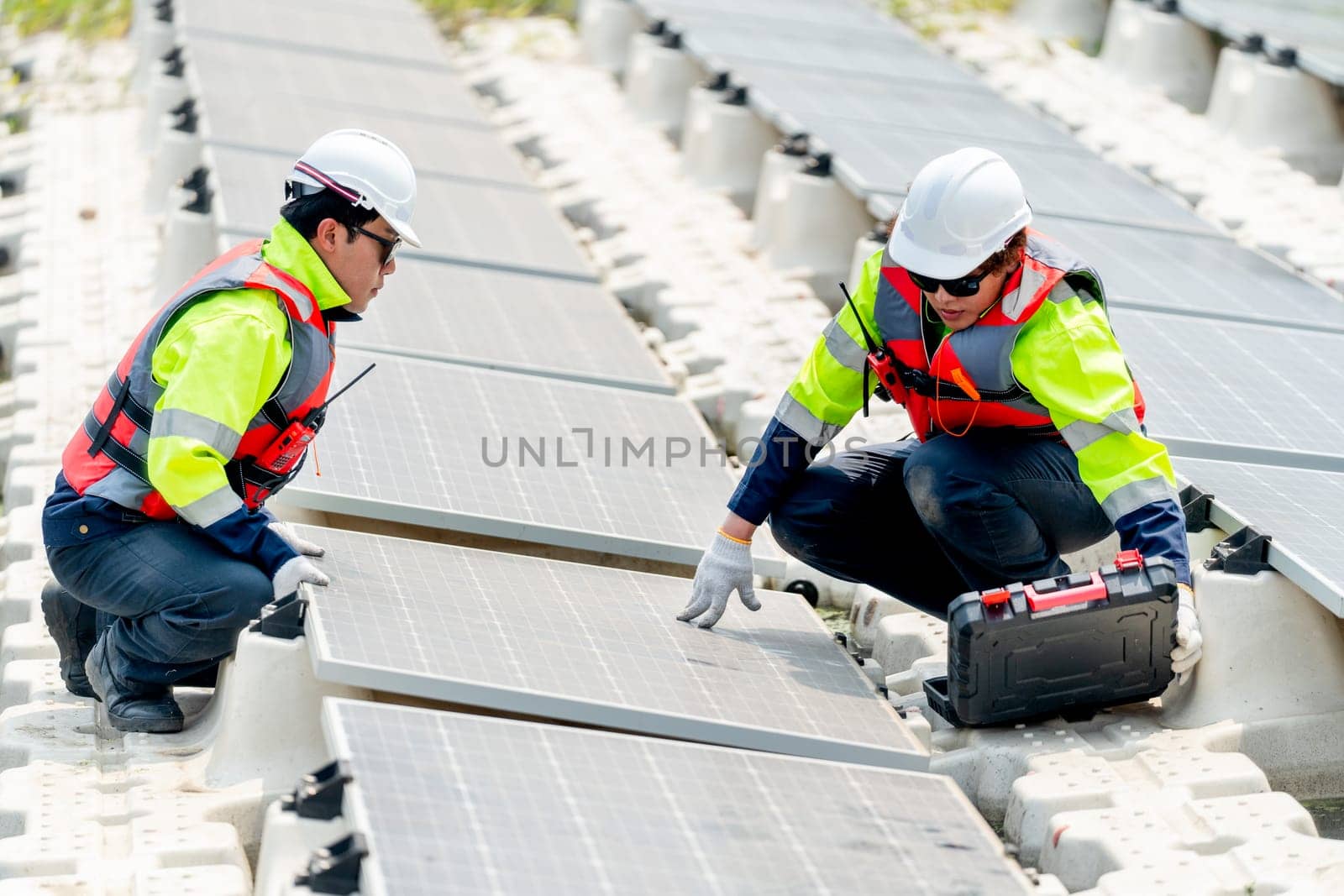 One professional technician worker sit and touch solar cell panel and discuss with co-worker for working  with system over the water reservoir. by nrradmin