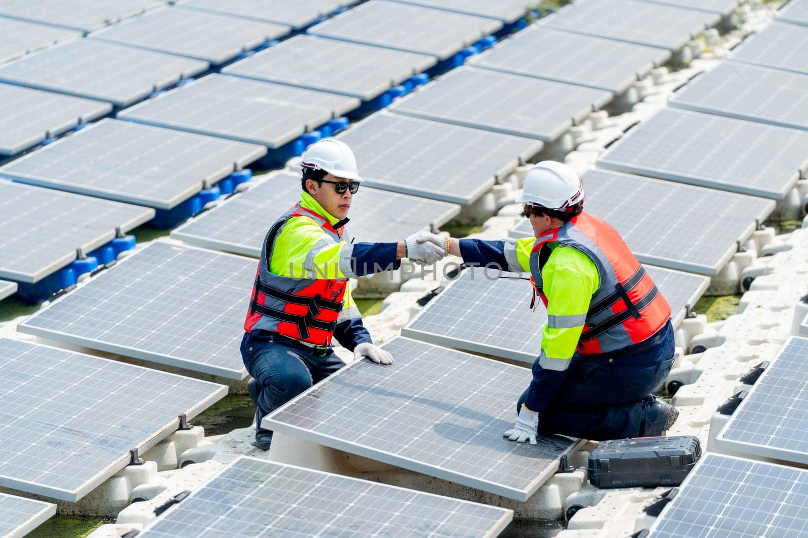 Two professional technician workers with safety uniform check hands for the success of work during work with solar cell panels system over water reservoir. by nrradmin