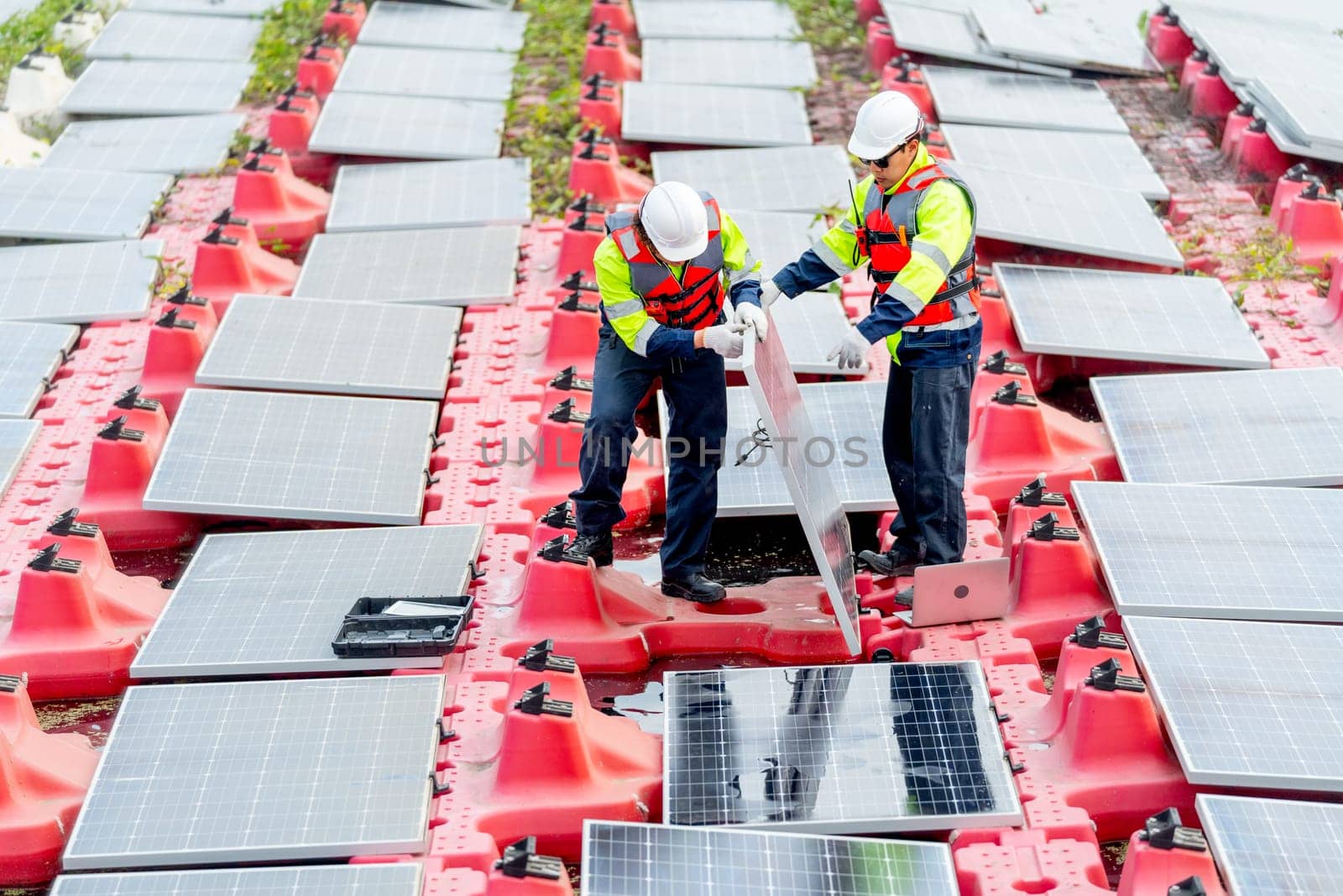 Professional technician workers hold solar cell panel during installation or set up into the system over water reservoir.