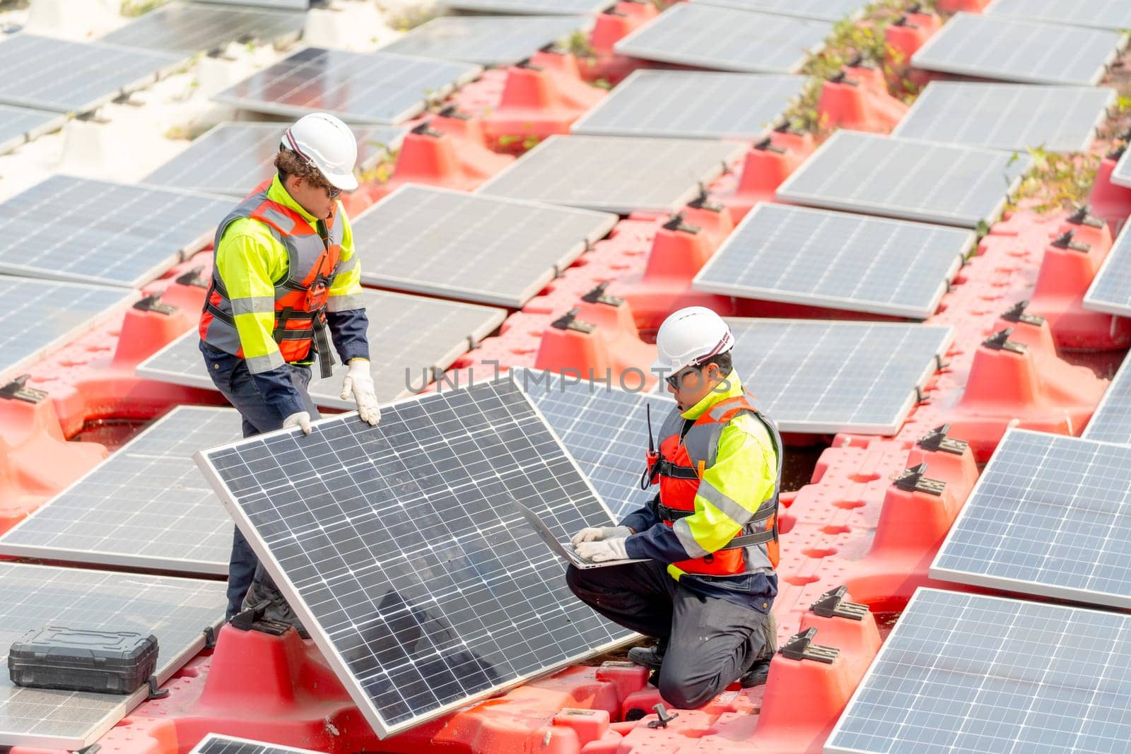 One technician worker stand with hold solar cell panel  and the other sit with check and maintenance the panels and stay on base over water reservoir.