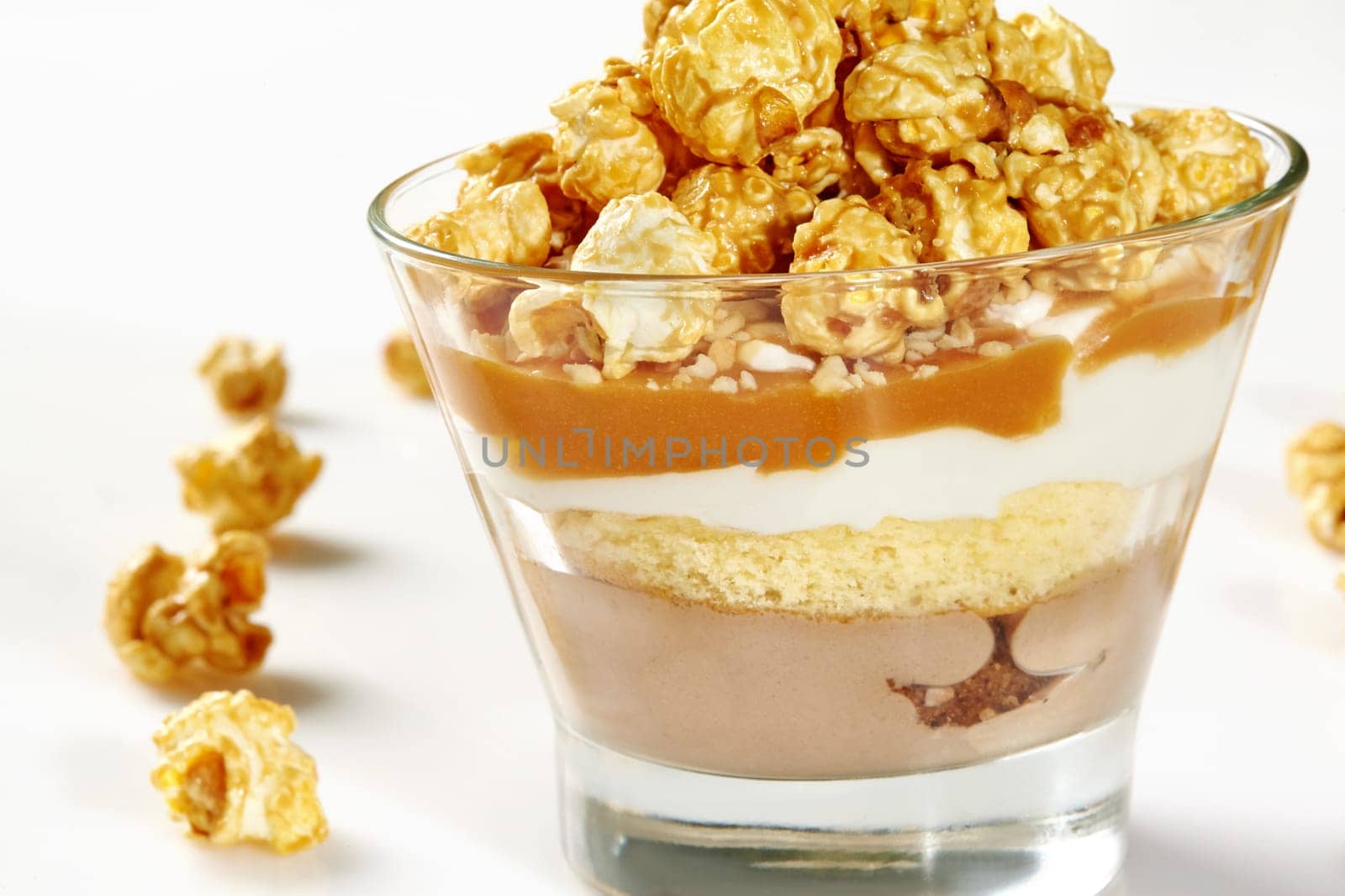 Glass of delicate layered dessert with ice cream, peanut crumbs, soft sponge cake, whipped cream and sweet caramel sauce decorated with crispy caramel-coated popcorn