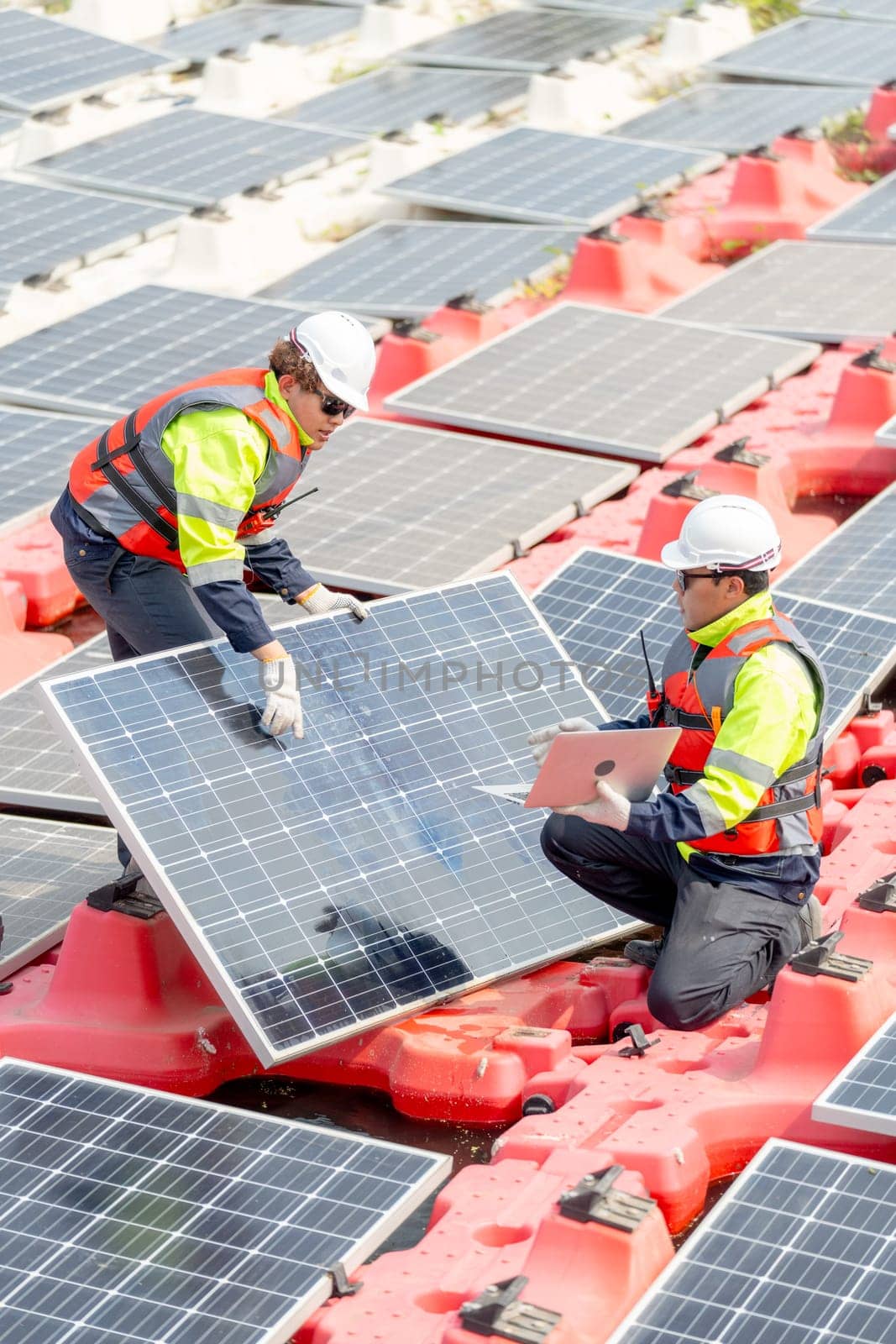 Vertical image of two technician workers help to check and maintenance solar cell panels that set up over area of water reservoir. by nrradmin