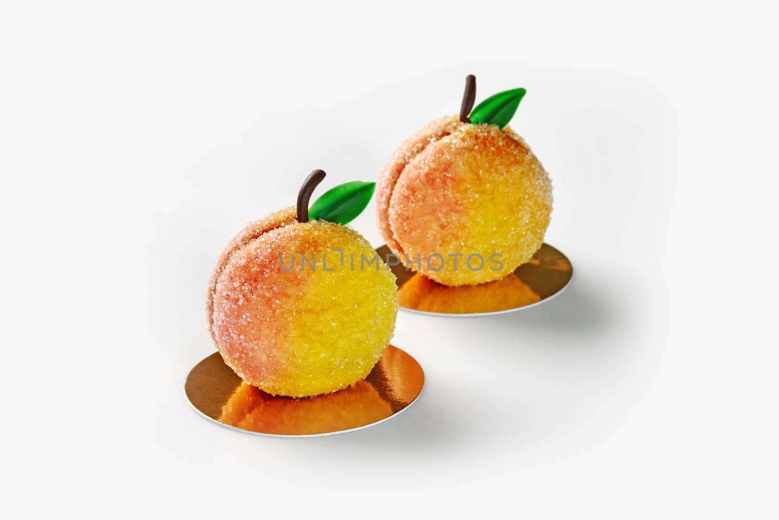 Two appetizing, dusted with sugar peach-shaped pastries with creamy mousse and pistachio sponge cake on golden cardboards against white background. Collections of signature handmade desserts