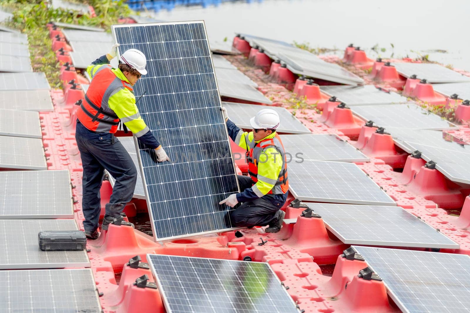 One of professional technician worker hold solar cell panel in vertical side also discuss with co-worker during work on base over water reservoir.