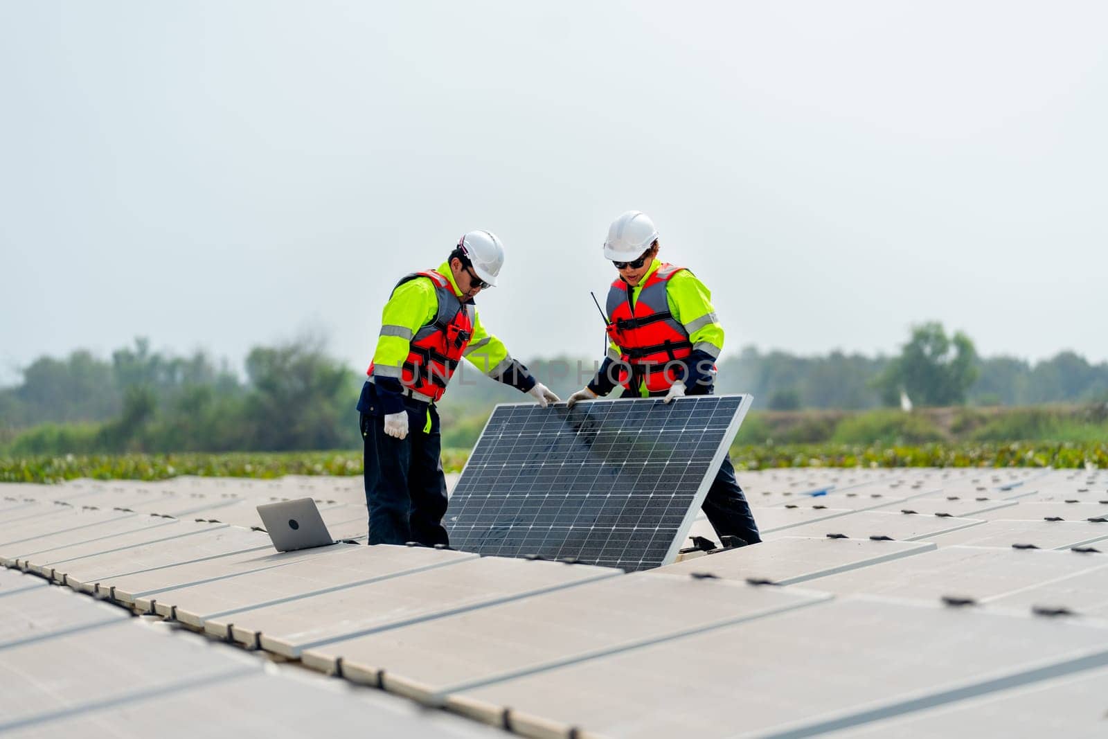 One technician worker stand and hold solar cell panel also work with co-worker who stand and touch to check the problem in the network system.