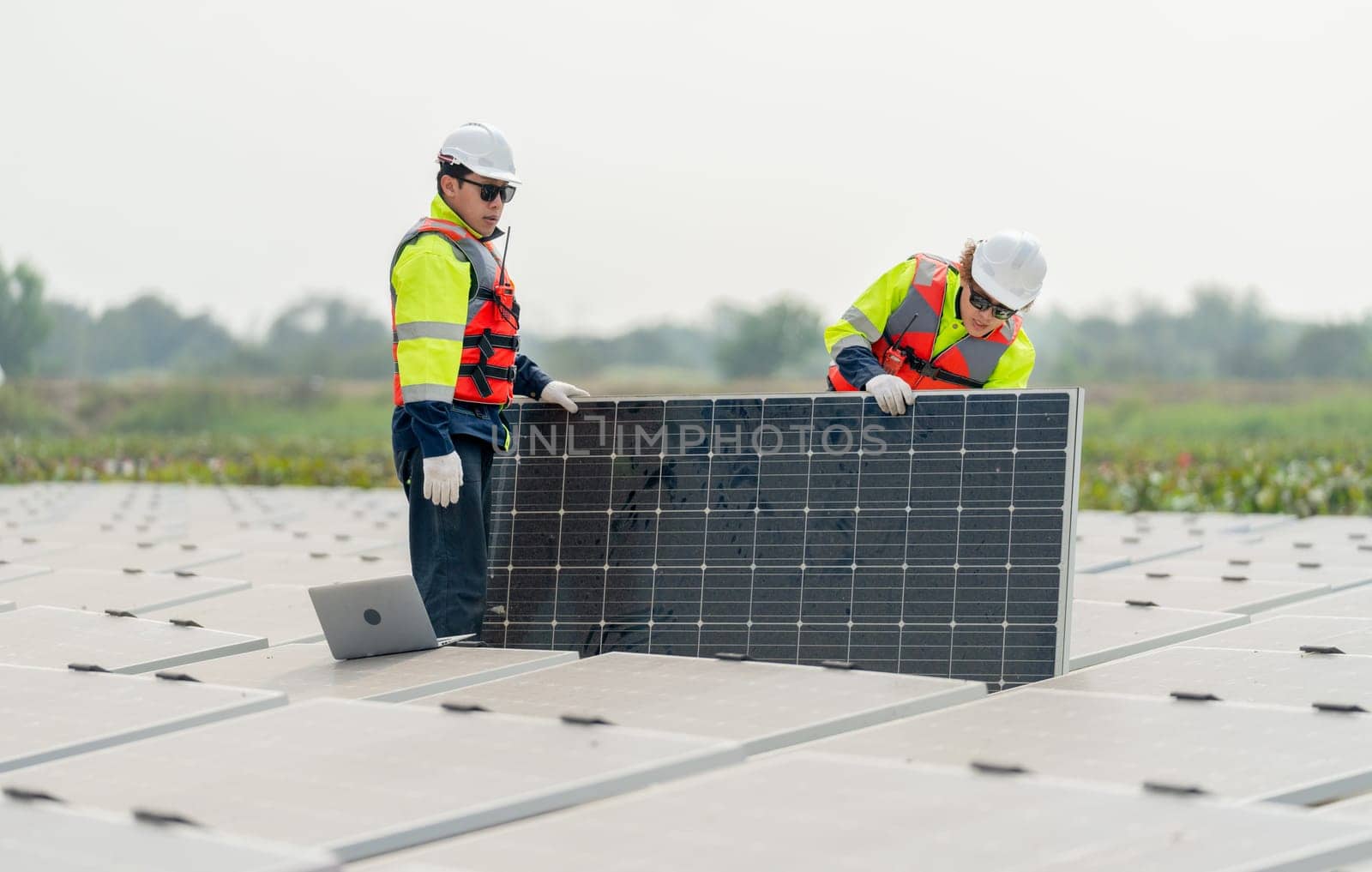 Two professional technician workers stand and hold solar cell panel in area of network of base over area of water reservoir. by nrradmin